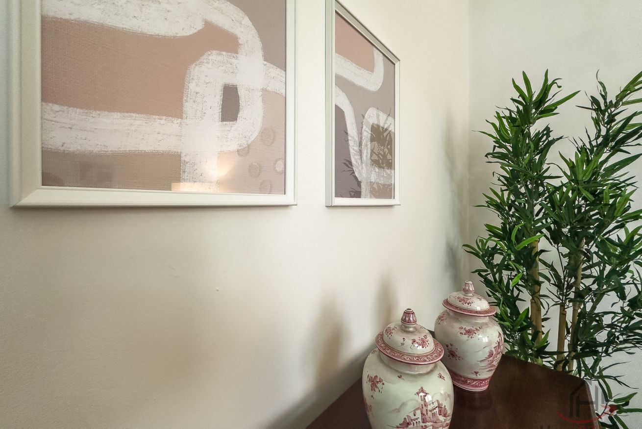 Deux tableaux abstraits encadrés, une plante en pot et deux vases en céramique sont posés sur une table.