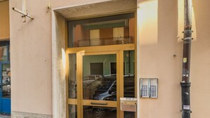 Una entrada de edificio con puerta de vidrio, escalera de metal y un cuadro eléctrico en la pared.