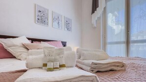 Una cama bien tendida con toallas dobladas, una mesita de noche con botellas y un cuadro en la pared.