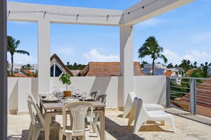 An outdoor patio with a table set for dining, surrounded by chairs, and a view of buildings and palm trees in the background. - Your very own oasis awaits you! (Bavaro)