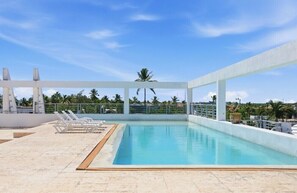 A rooftop swimming pool with lounge chairs, a palm tree, and a clear sky. - Your very own oasis awaits you! (Bavaro)