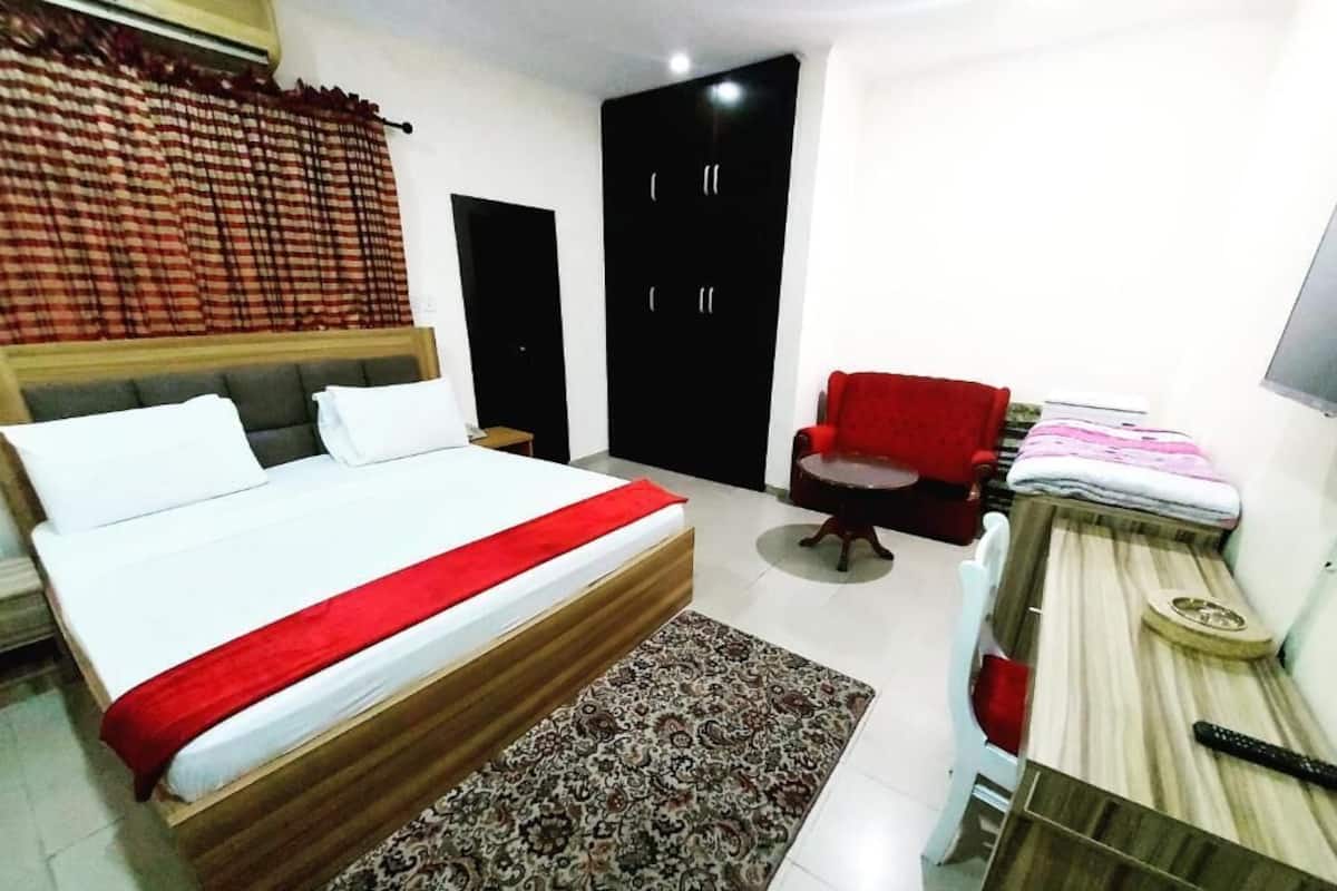 Une chambre d’hôtel avec un lit, une chaise rouge, un bureau et une armoire.