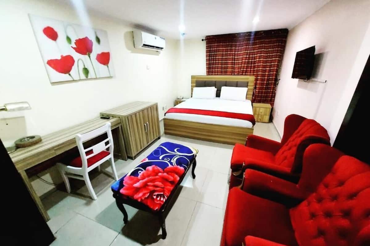 Une chambre avec un lit, un bureau, une chaise, une télévision et un canapé rouge.