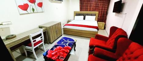 A bedroom with a bed, a desk, a chair, a TV, and a red sofa.