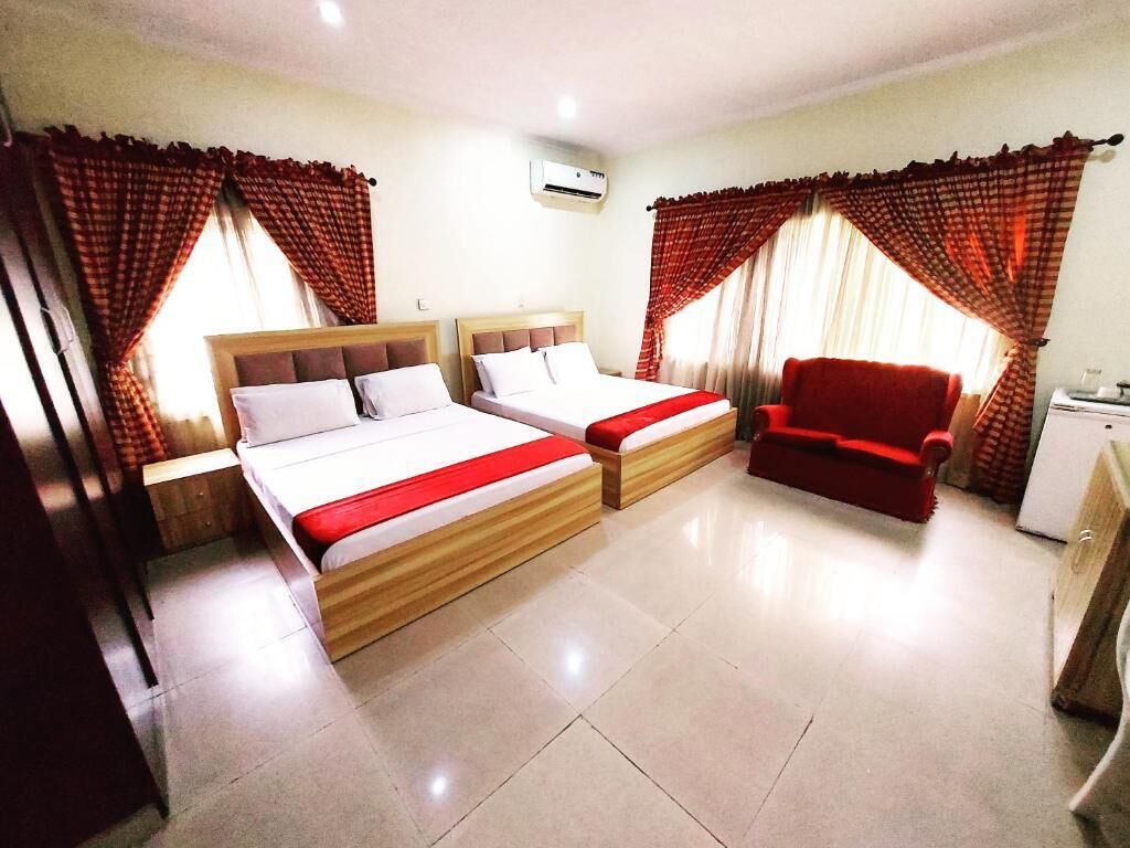 A hotel room with two beds, a red chair, a desk, and curtains.