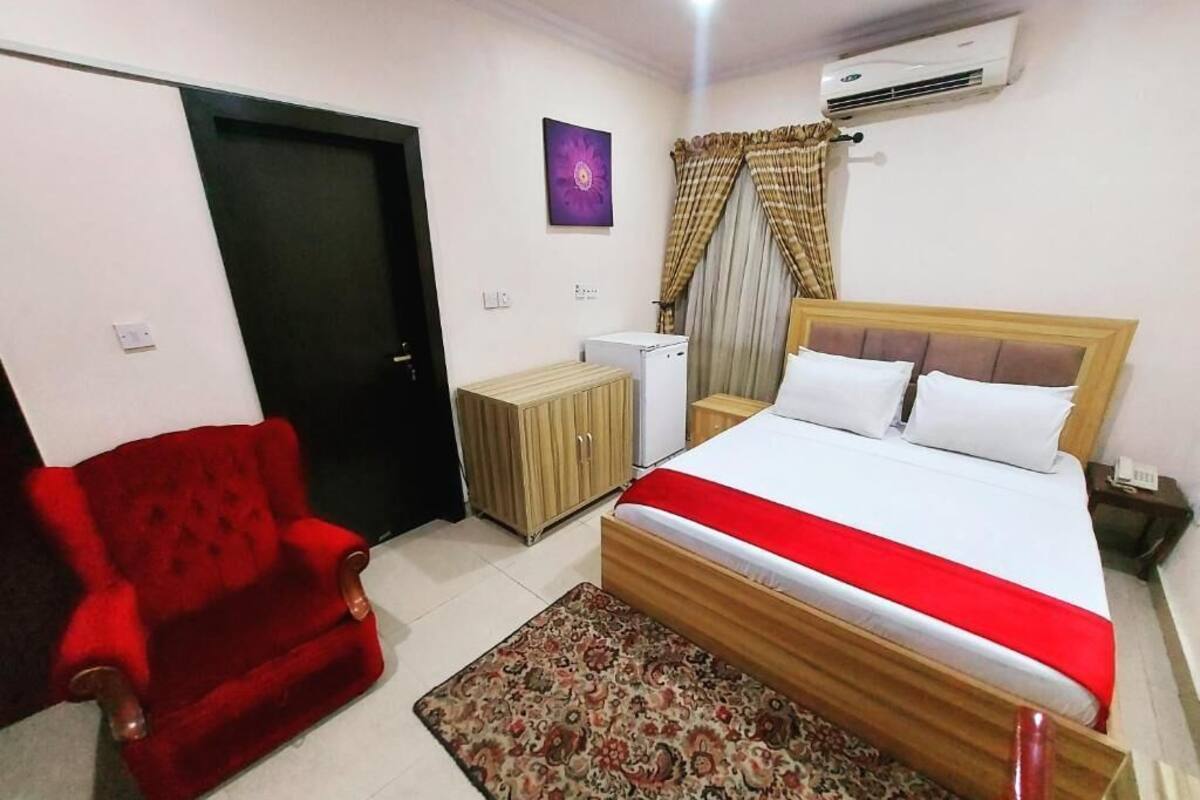 Une chambre à coucher avec un lit, un fauteuil rouge, une armoire et un appareil de climatisation.