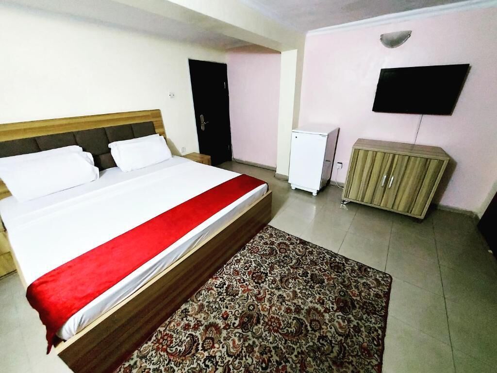 A hotel room with a bed, a television, a refrigerator, and a cabinet.