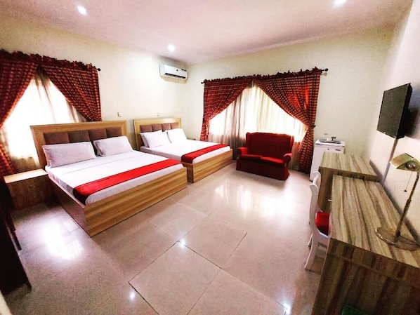 Habitación de hotel con dos camas, un sillón rojo, un escritorio con lámpara y una televisión.