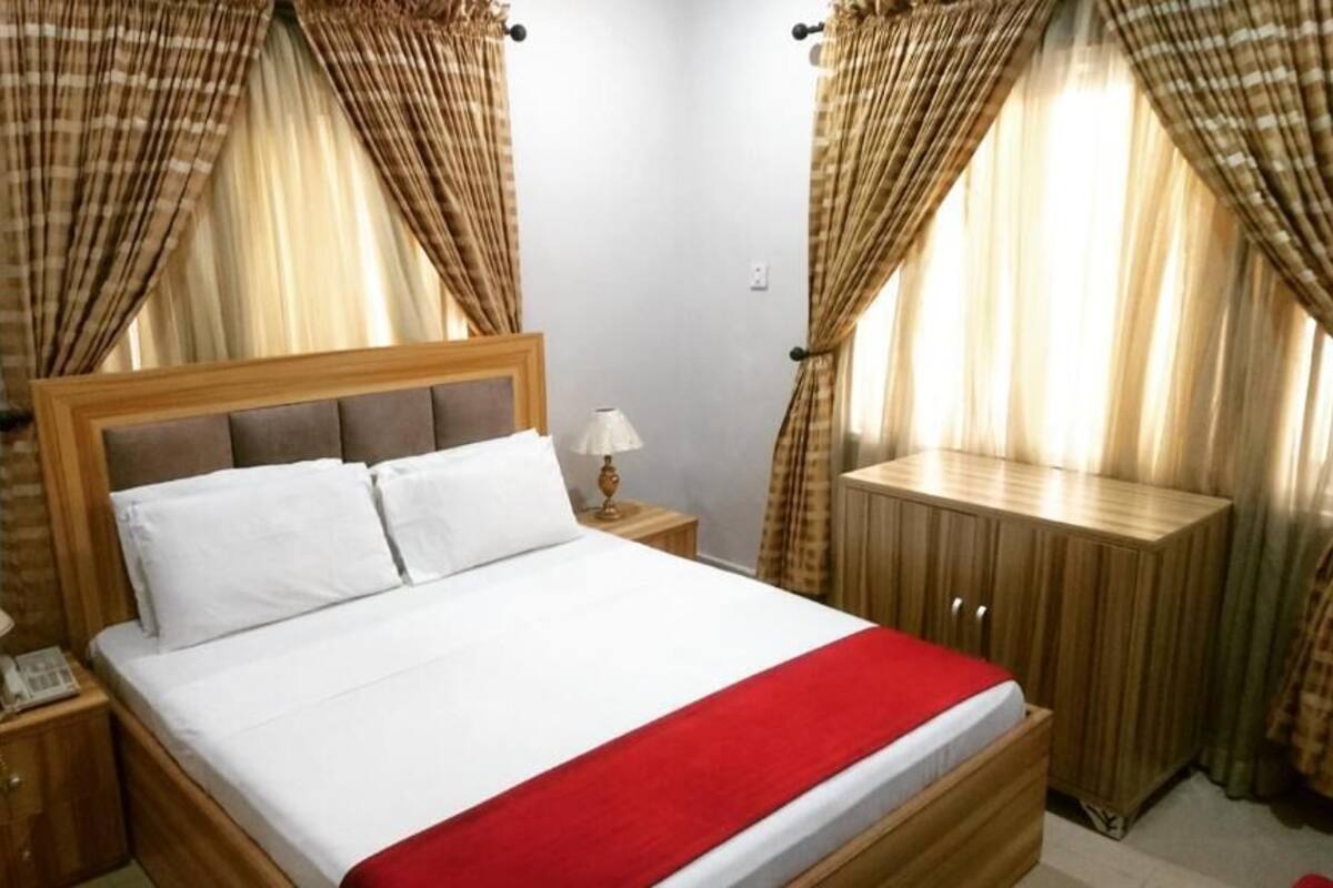 Un lit avec une tête de lit en bois, une table de chevet avec une lampe et une petite table de nuit avec un téléphone.