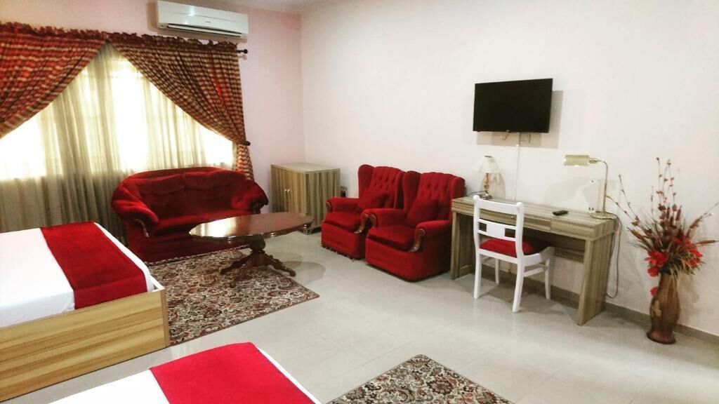 A room with a bed, a desk, a chair, two red sofas, a TV, and a plant.