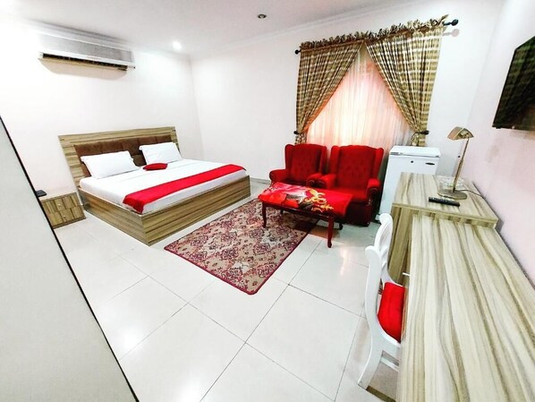 A hotel room with a bed, a red armchair, a small table, and a desk.