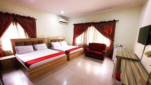 Una habitación de hotel con dos camas, un sillón rojo, un escritorio y una televisión.