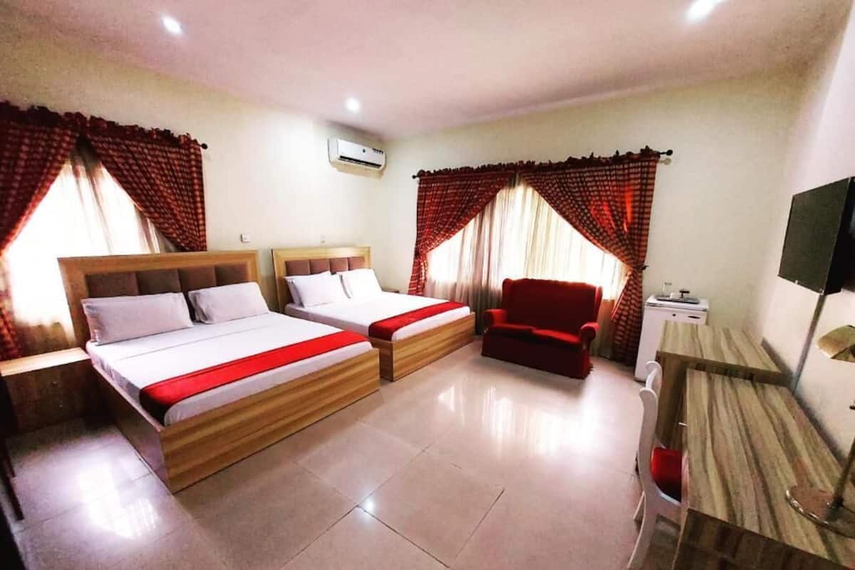 Une chambre d’hôtel avec deux lits, un fauteuil rouge, un bureau et une télévision.
