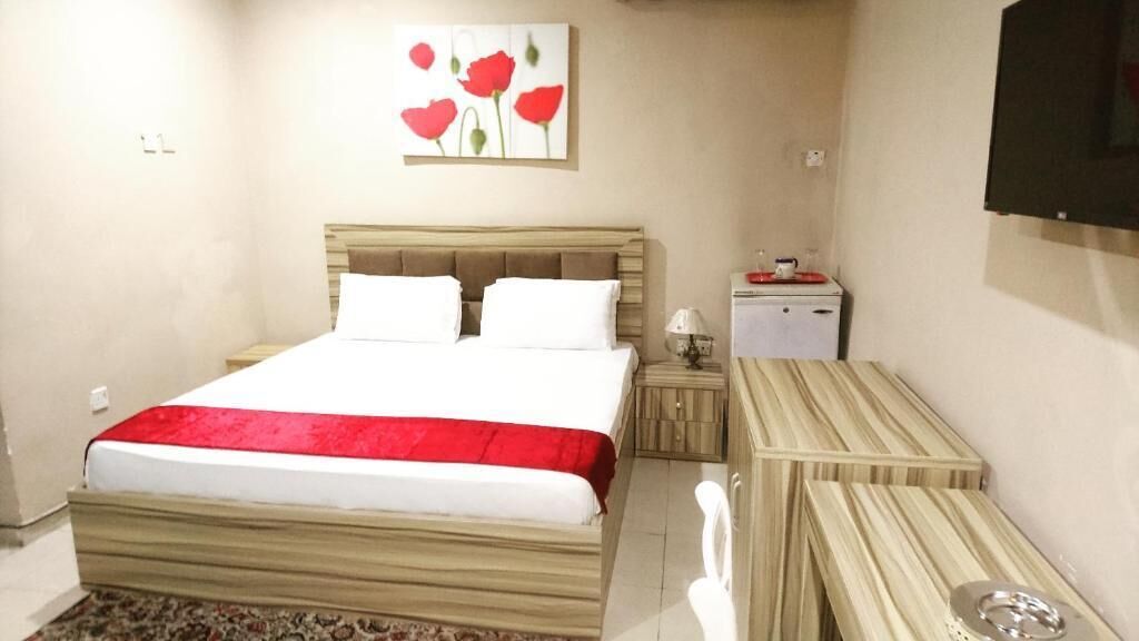 Une chambre à coucher comprenant un lit, des tables de chevet, un petit bureau, un miroir et un téléviseur fixé au mur.
