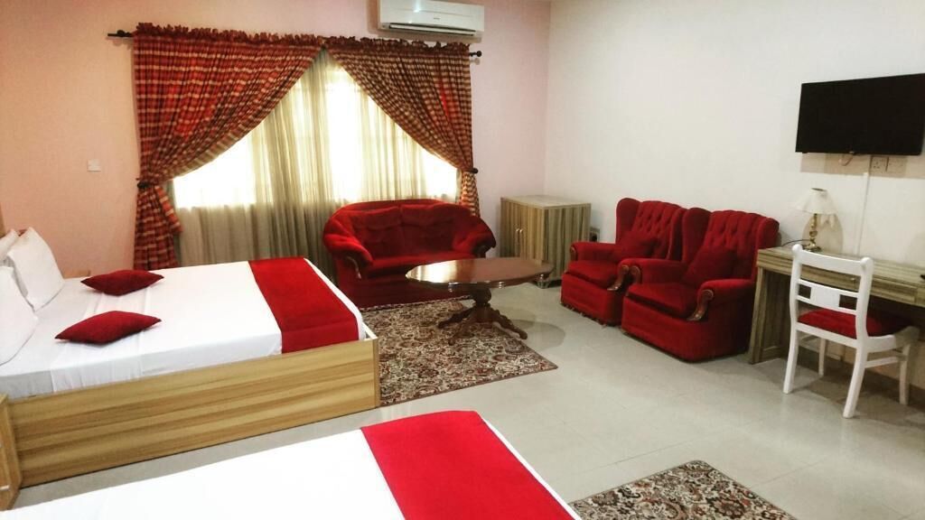 A hotel room with a bed, two red sofas, a small table, a TV, and a desk with a chair.