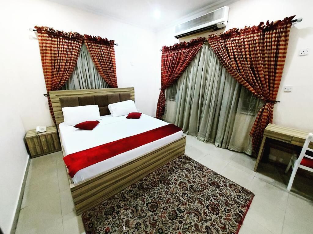 A bedroom with a bed, a bedside table, an air conditioner, and a patterned rug.