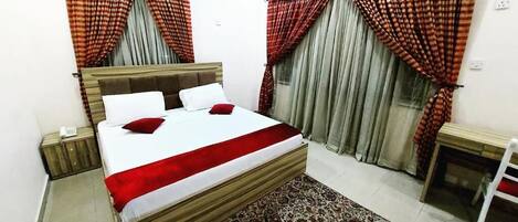 A bedroom with a bed, a bedside table, an air conditioner, and a patterned rug.