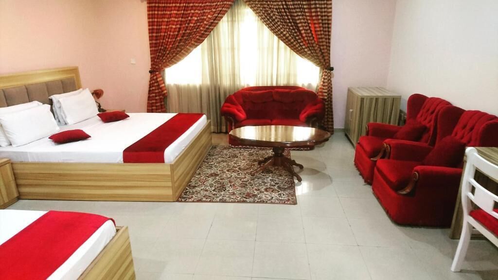 Une chambre d’hôtel avec un lit, un canapé rouge, une petite table ronde et un fauteuil rouge.