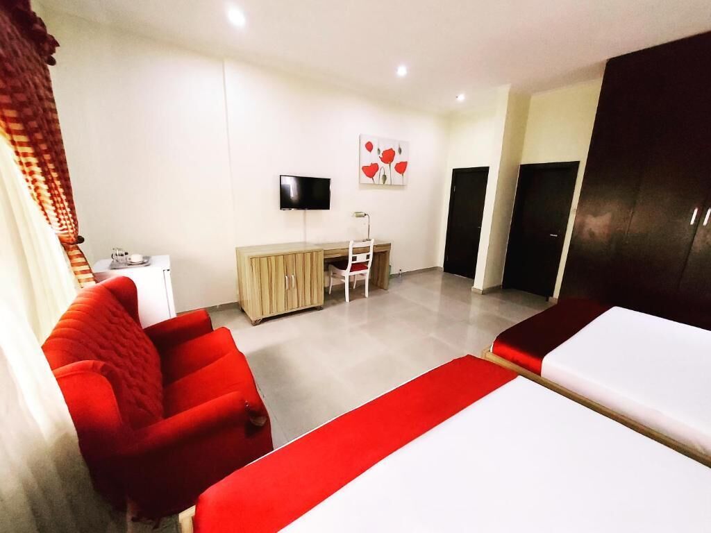 Een hotelkamer met een bed, een rode fauteuil, een bureau, een televisie en een kledingkast.
