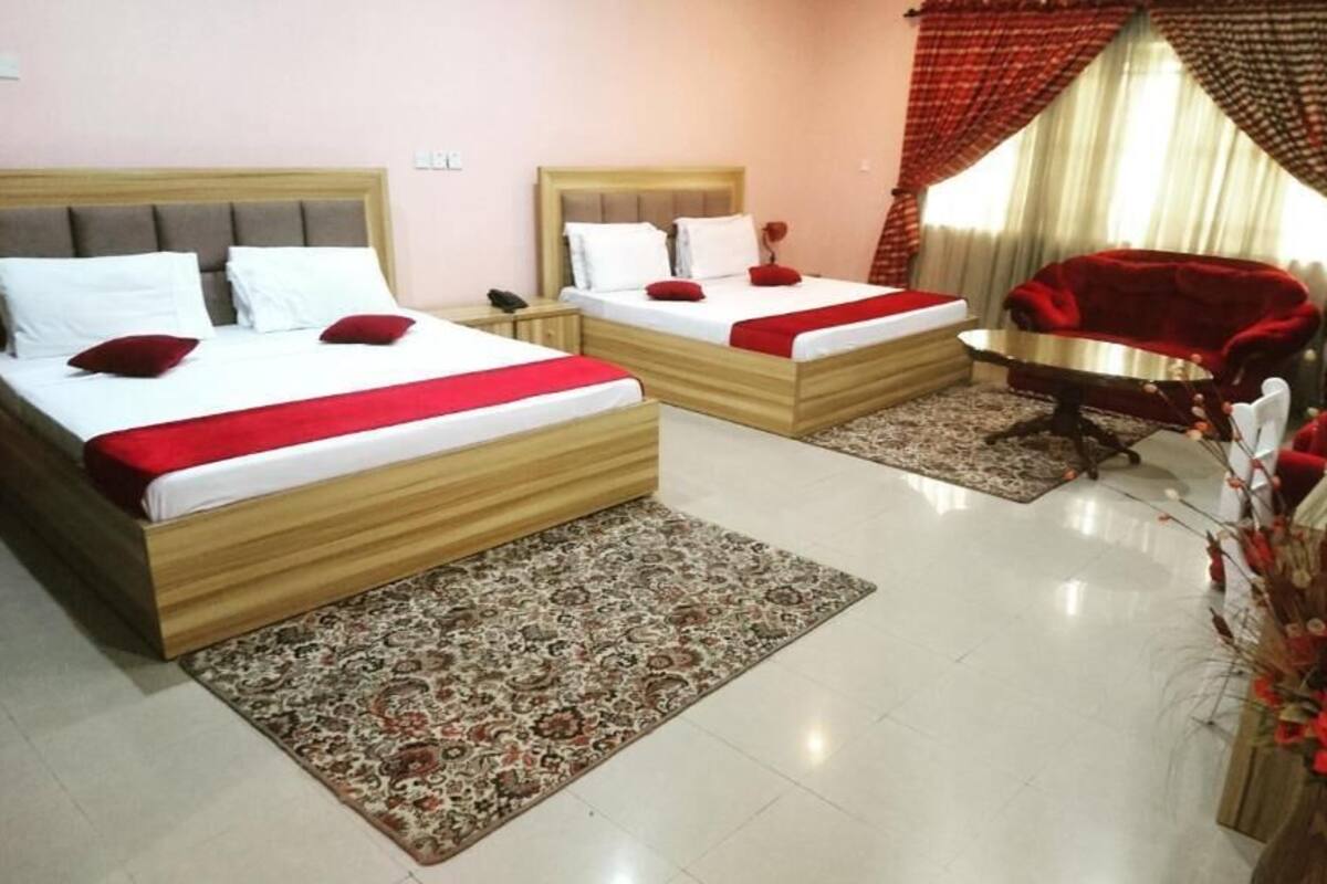 Une chambre d’hôtel avec deux lits, un canapé rouge, une table à manger et un vase décoratif.