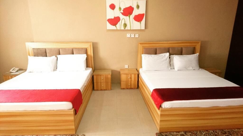 Two double beds with wooden headboards, a red throw blanket, and a wall-mounted painting of red flowers.