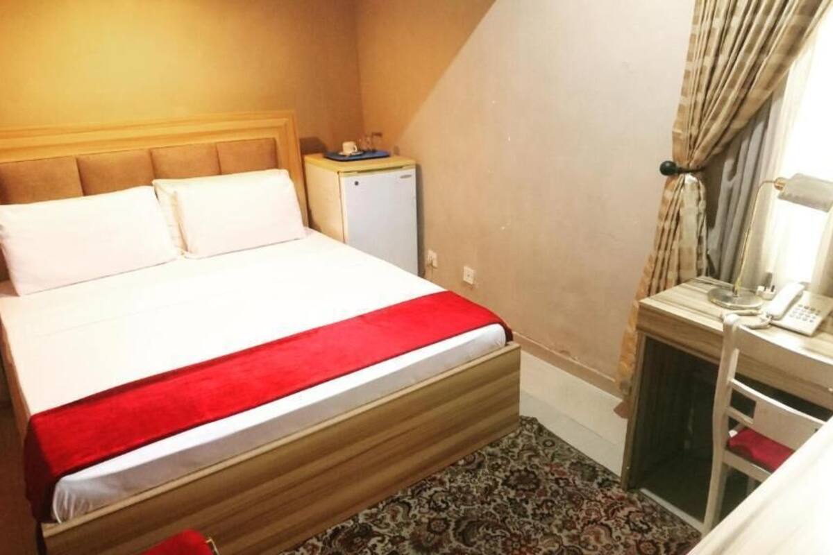Une chambre d’hôtel équipée d’un lit, d’un bureau, d’un téléphone et d’un petit réfrigérateur.