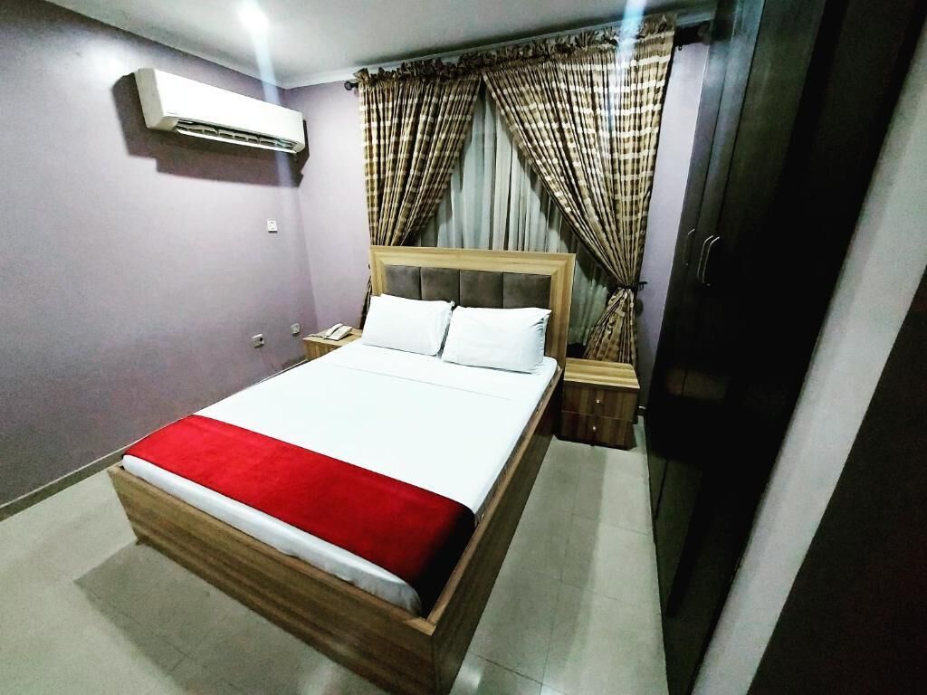 A bedroom with a bed, curtains, an air conditioning unit, and a wooden nightstand.