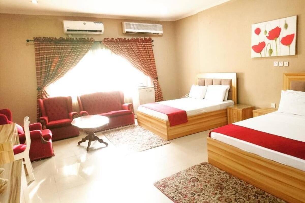 Une chambre d’hôtel avec deux lits, un canapé, une petite table et une fenêtre avec des rideaux.