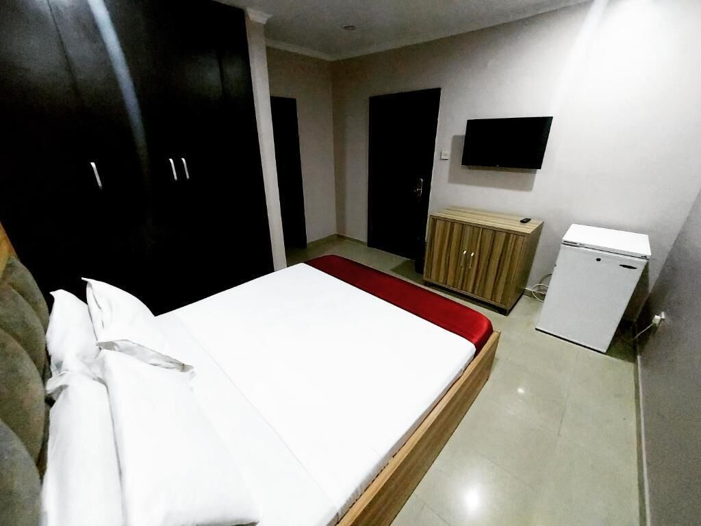 A bedroom with a bed, a wardrobe, a television, and a small refrigerator.