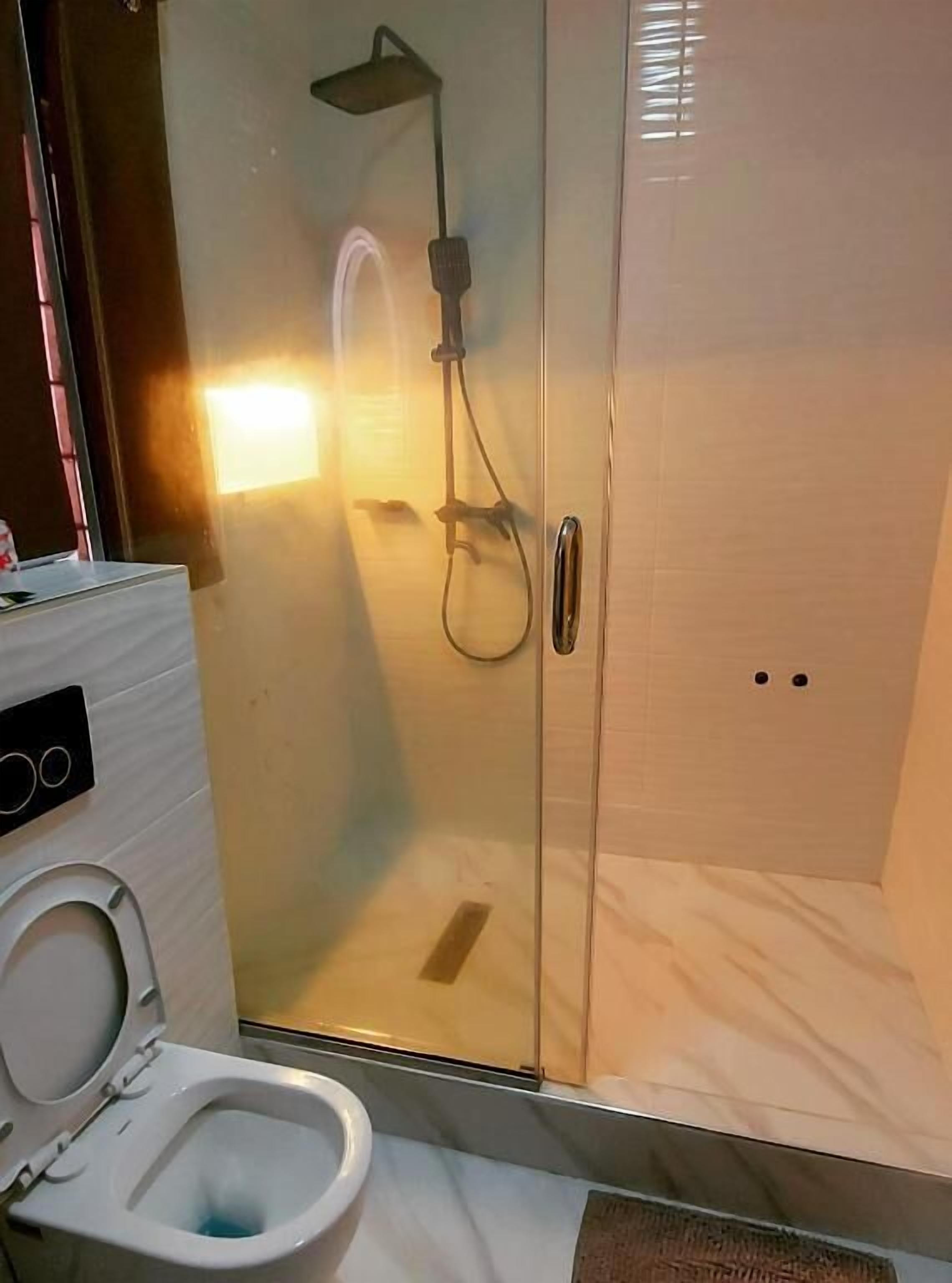 A bathroom with a glass-enclosed shower, a toilet, and a wall-mounted control panel.