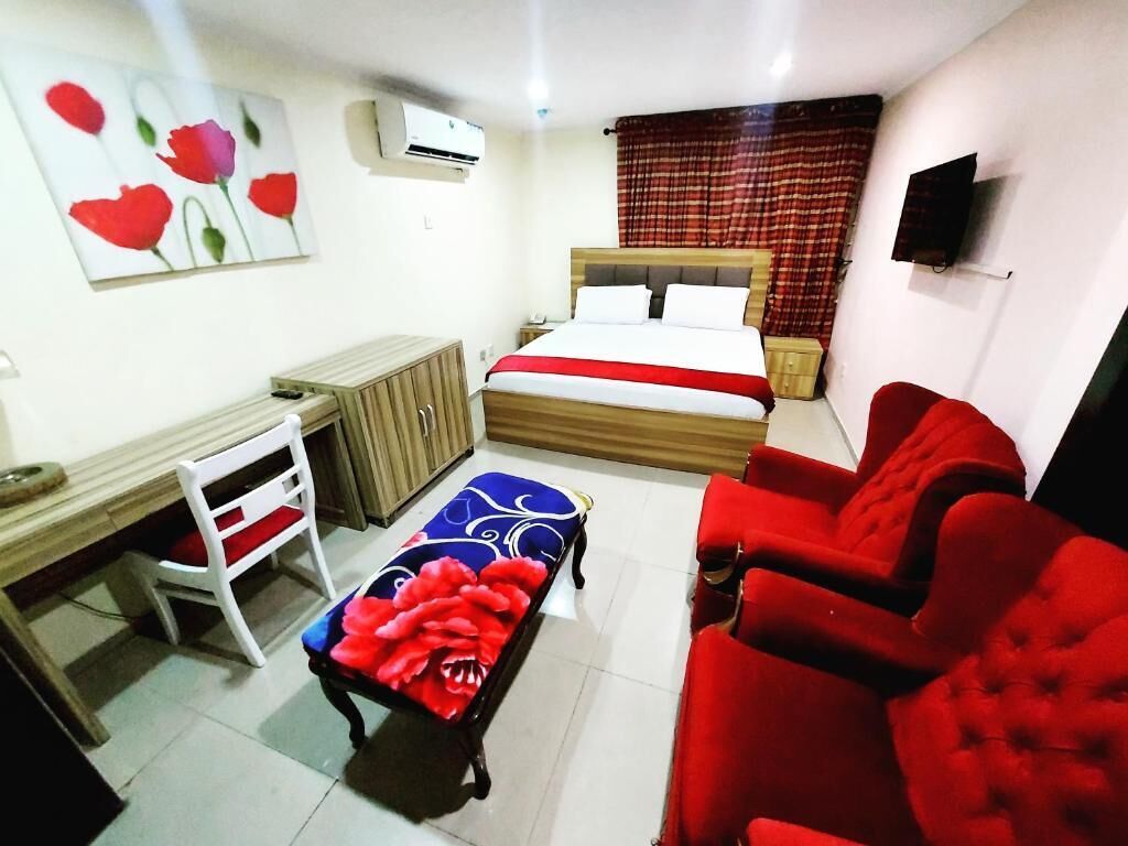 A bedroom with a bed, a desk, a chair, a sofa, and a TV.
