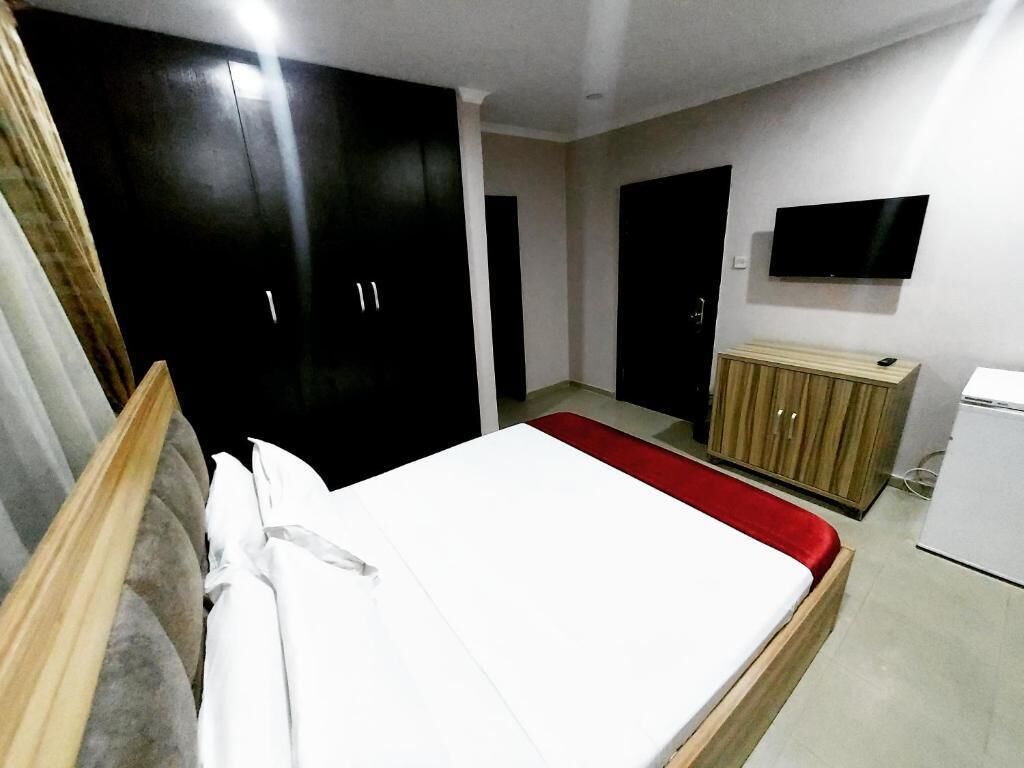 A bedroom with a bed, wardrobe, television, and a small refrigerator.