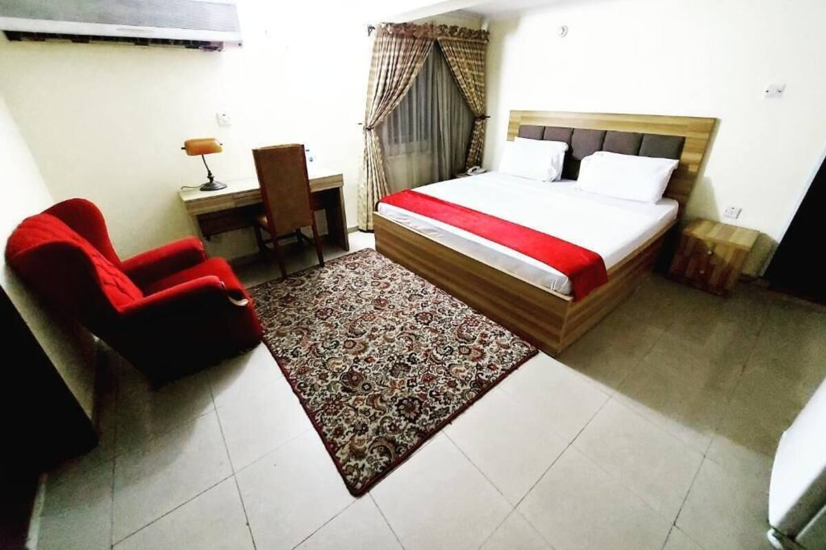 Une chambre d’hôtel avec un lit, un bureau, une chaise, un tapis et des rideaux.
