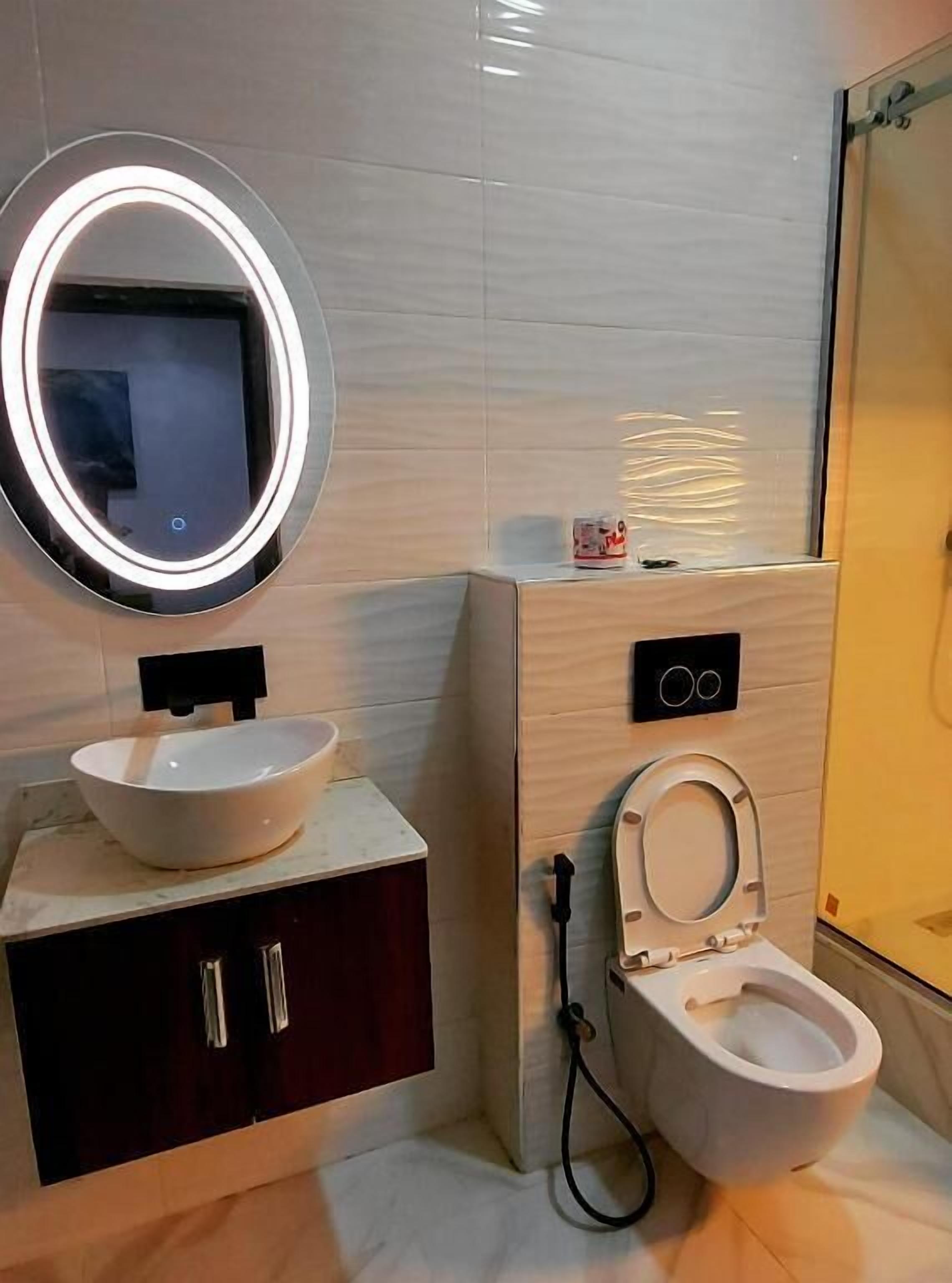 Un baño con lavamanos blanco, un espejo redondo con iluminación, inodoro y zona de ducha.