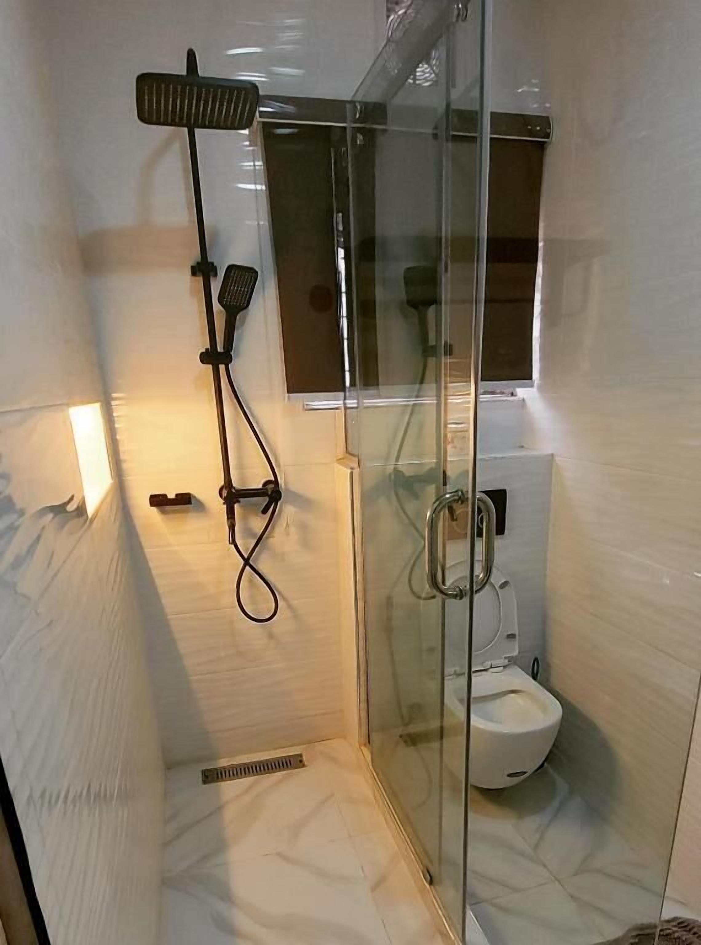 A modern bathroom with a glass shower enclosure, a toilet, and a hand dryer.