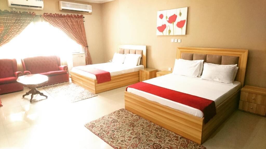 A hotel room with two beds, a sofa, a small table, and a patterned rug.
