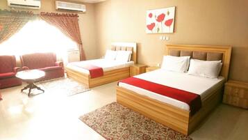 A hotel room with two beds, a sofa, a small table, and a patterned rug.