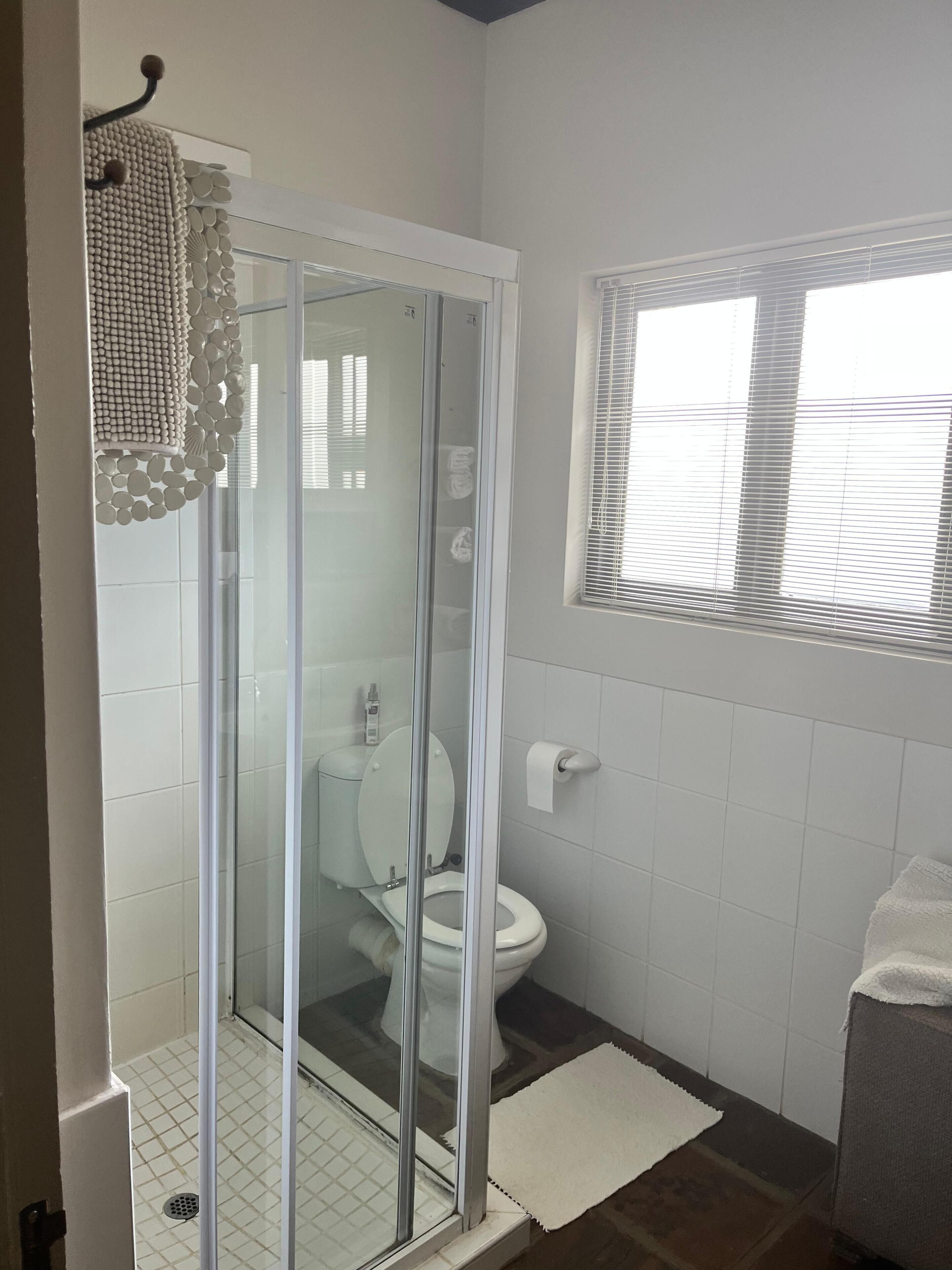 Ein Badezimmer mit Duschkabine, Toilette und einem Fenster mit Jalousien.