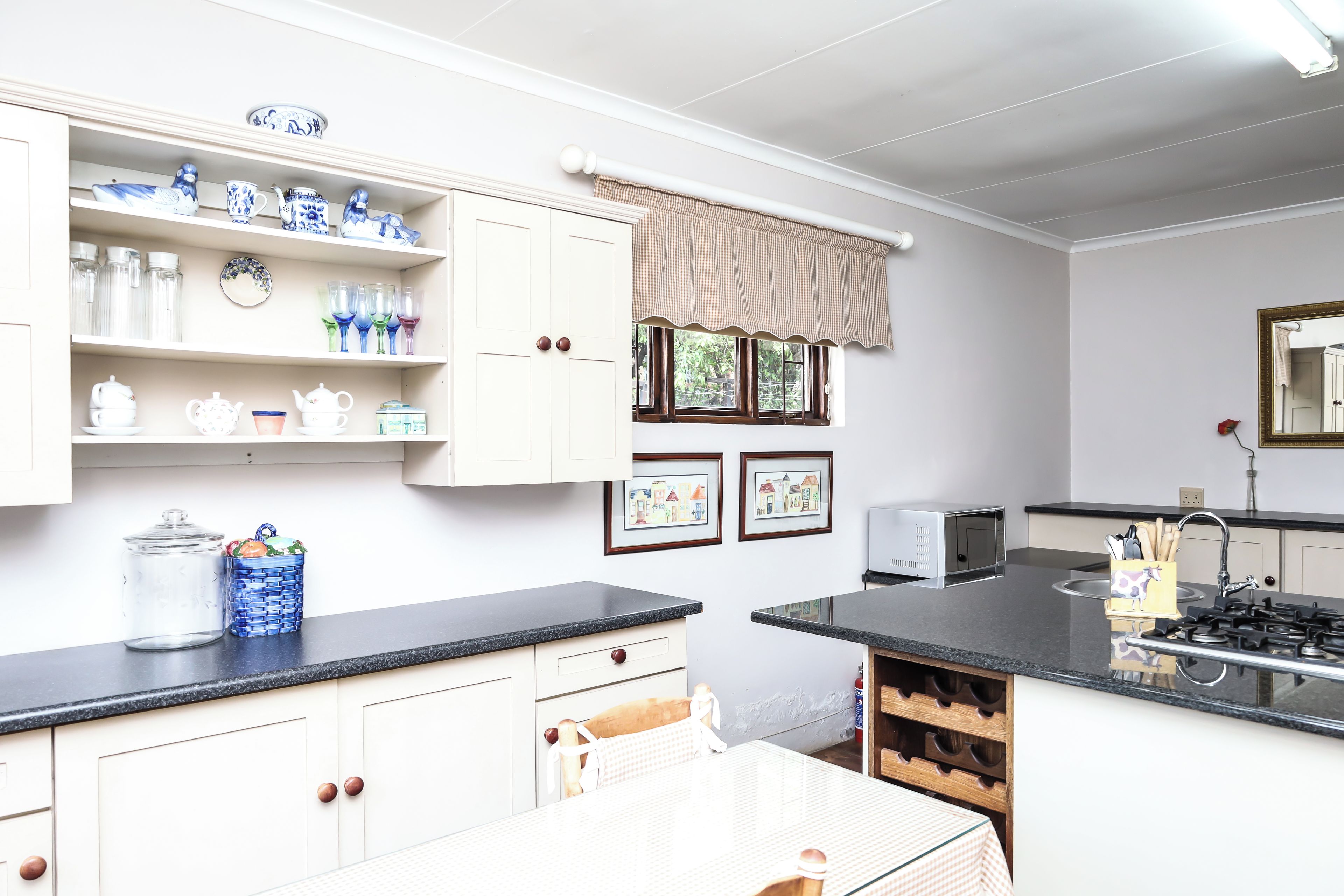A kitchen with white cabinets, a black countertop, and a window with a checkered valance.