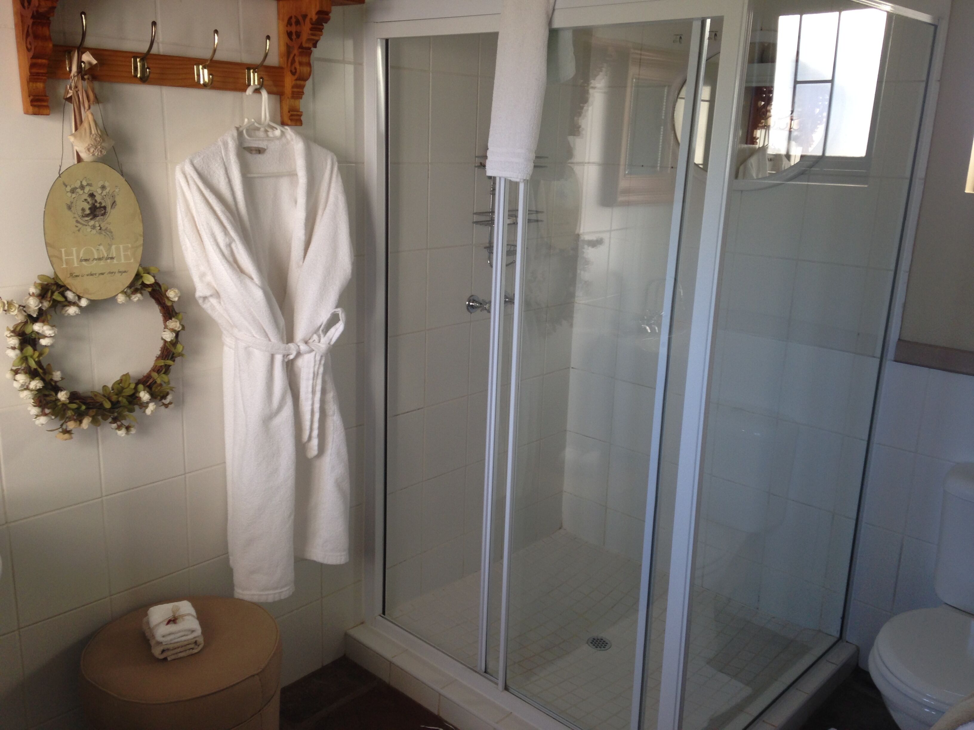 A bathroom with a glass-enclosed shower, a toilet, and a towel rack with a decorative wreath.