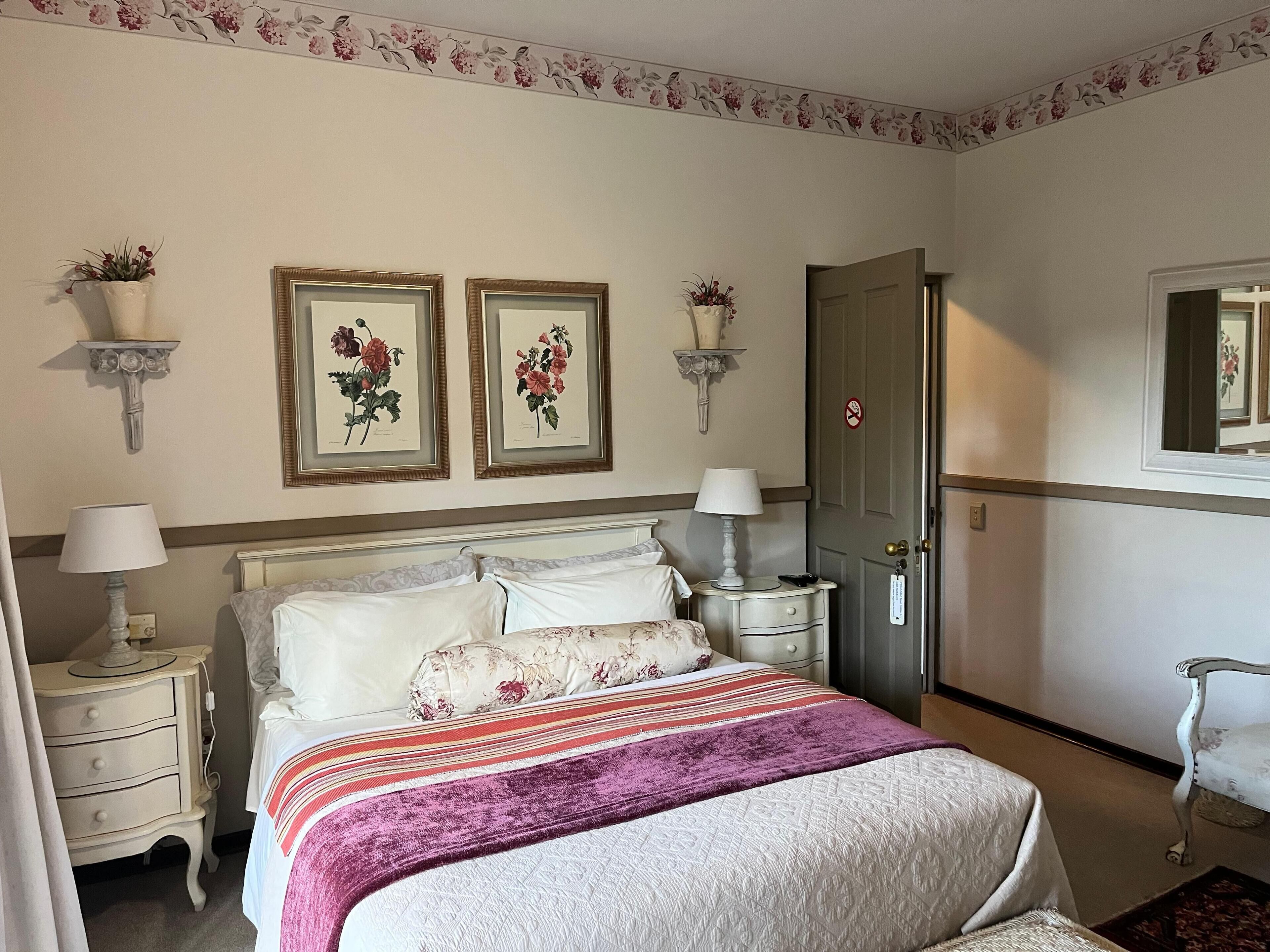 A neatly arranged bedroom with a bed, two bedside tables, a nightstand, a door, and a chair.