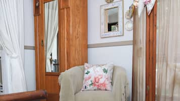 A room with a wooden cabinet, a sofa with floral cushions, a television on a stand, and a patterned rug.