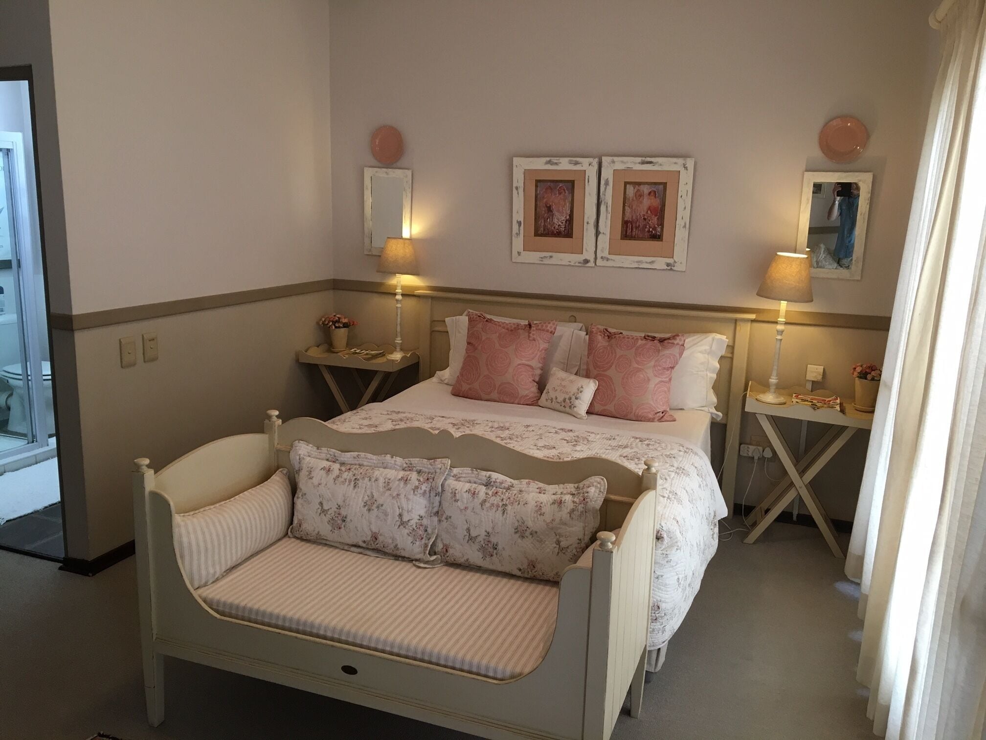 A bedroom with a bed, bedside tables, lamps, a mirror, and two framed pictures on the wall.
