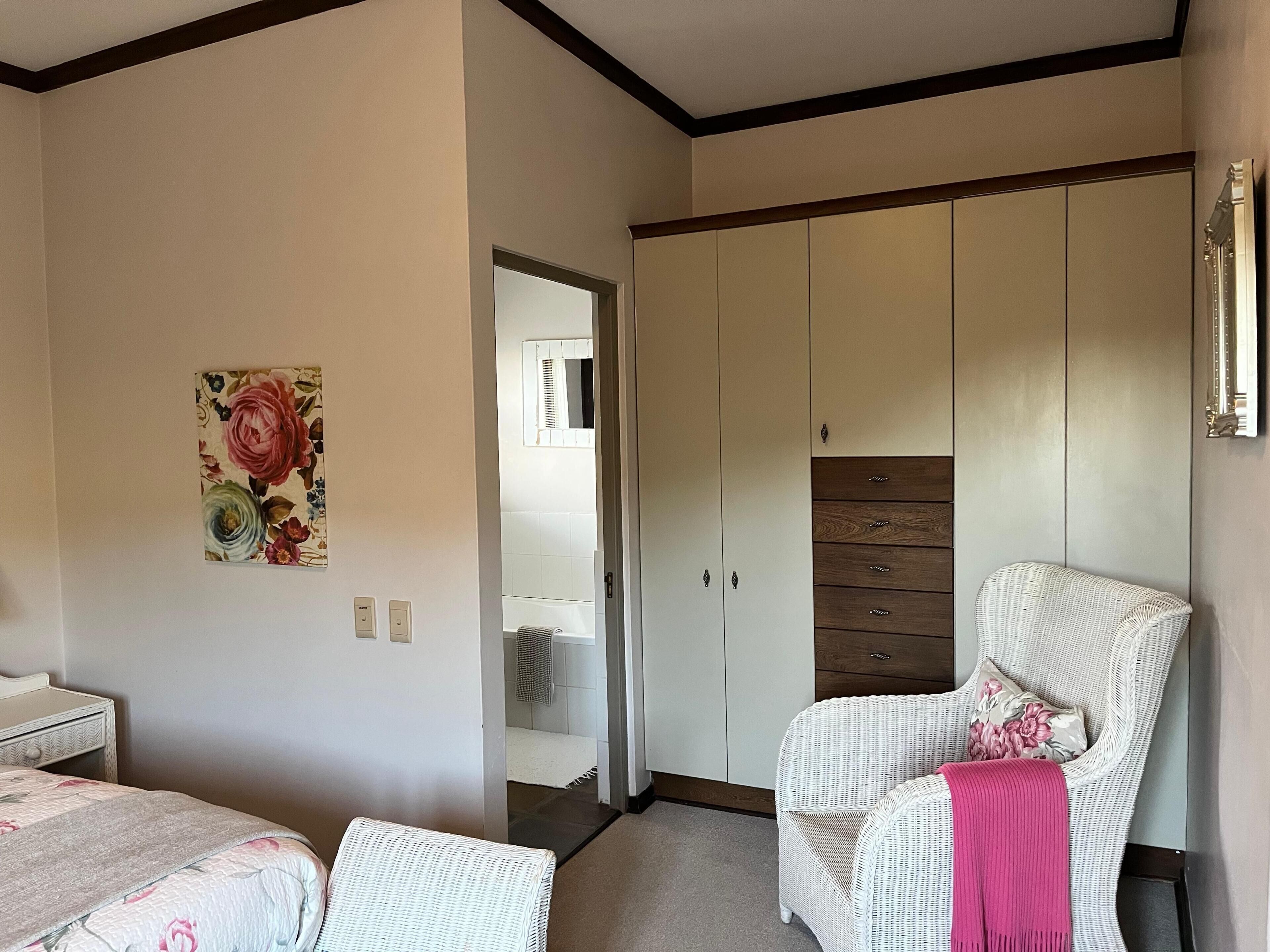 A bedroom with a bed, a chair, a wardrobe, and a floral painting on the wall.