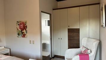 Un dormitori amb un llit, una cadira, un armari i un quadre floral a la paret.
