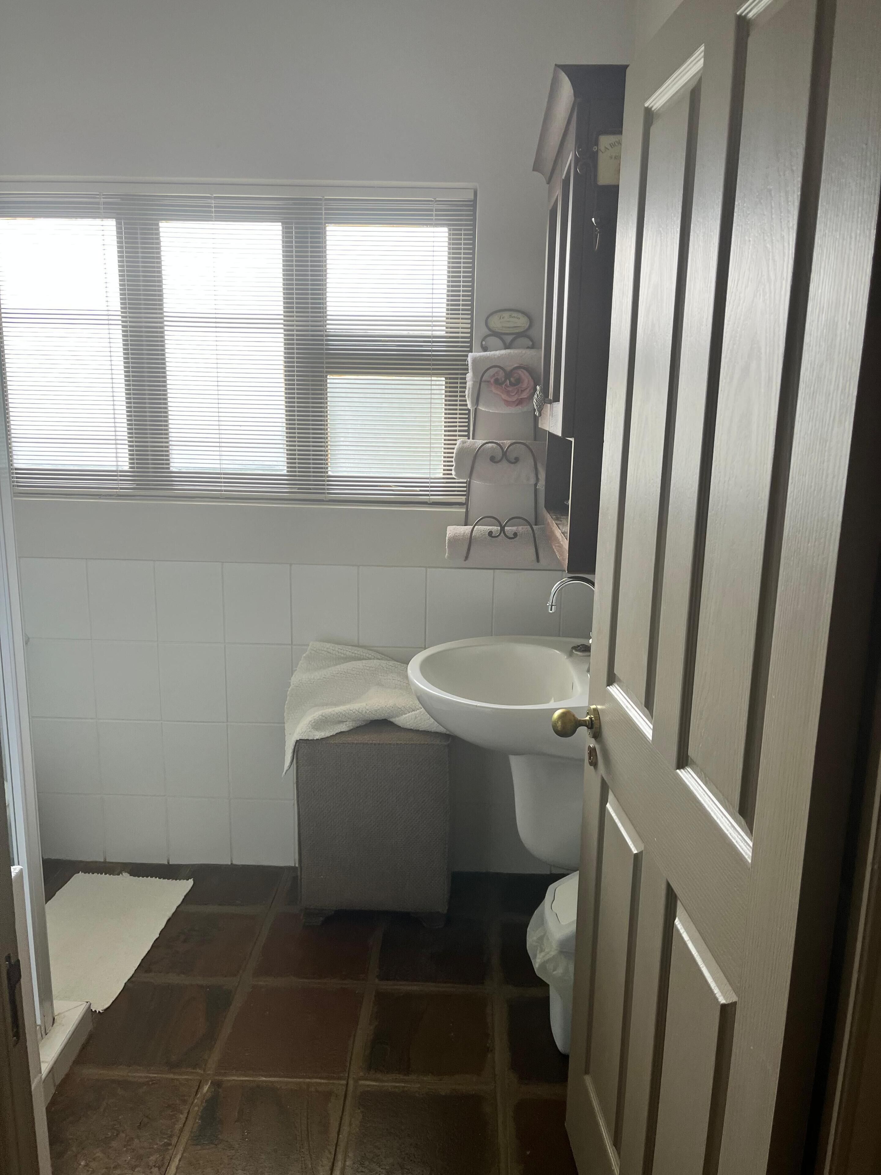 Un baño con lavamanos, inodoro y ventana con persianas.