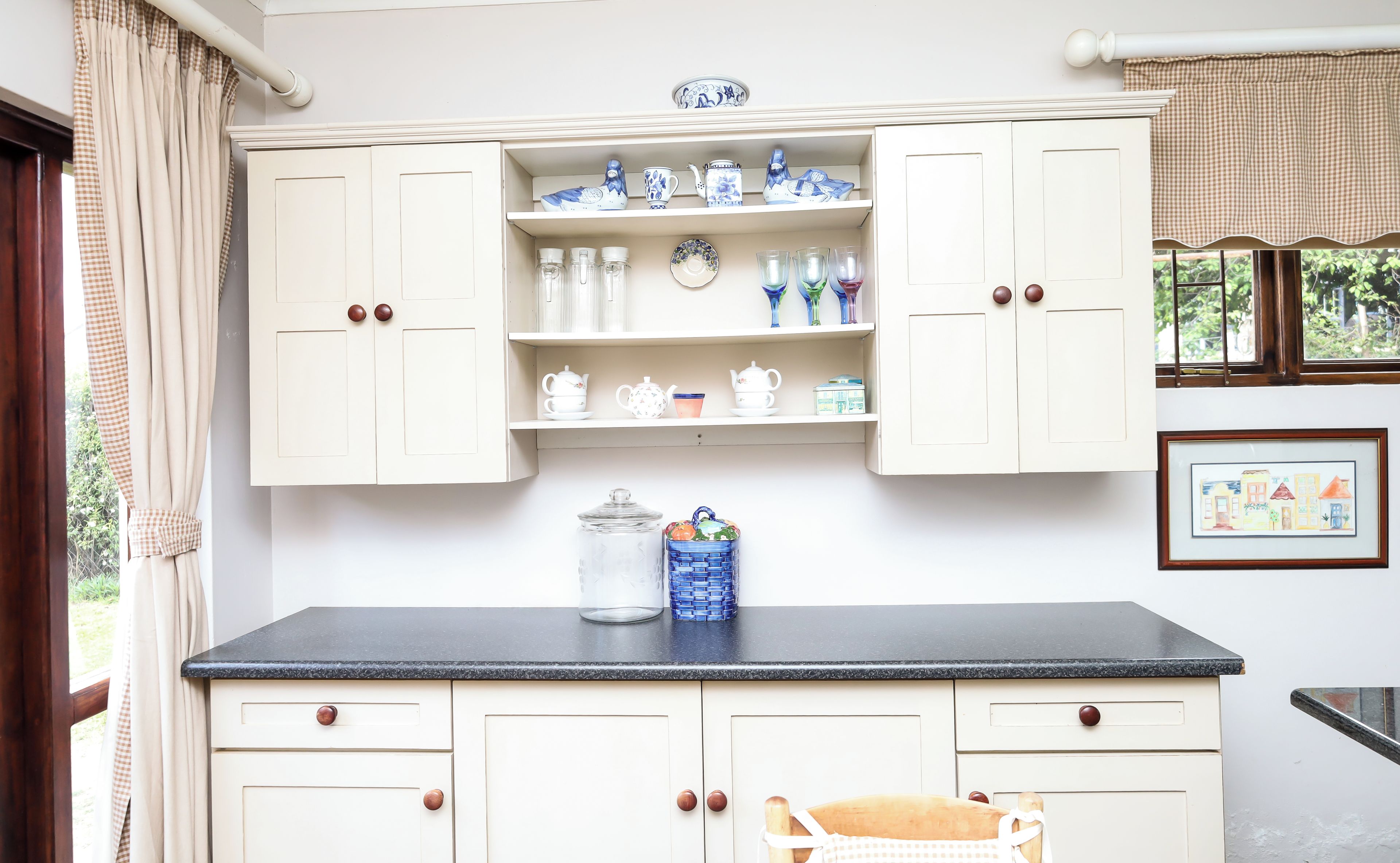 A kitchen with white cabinetry, a black countertop, and various kitchenware.