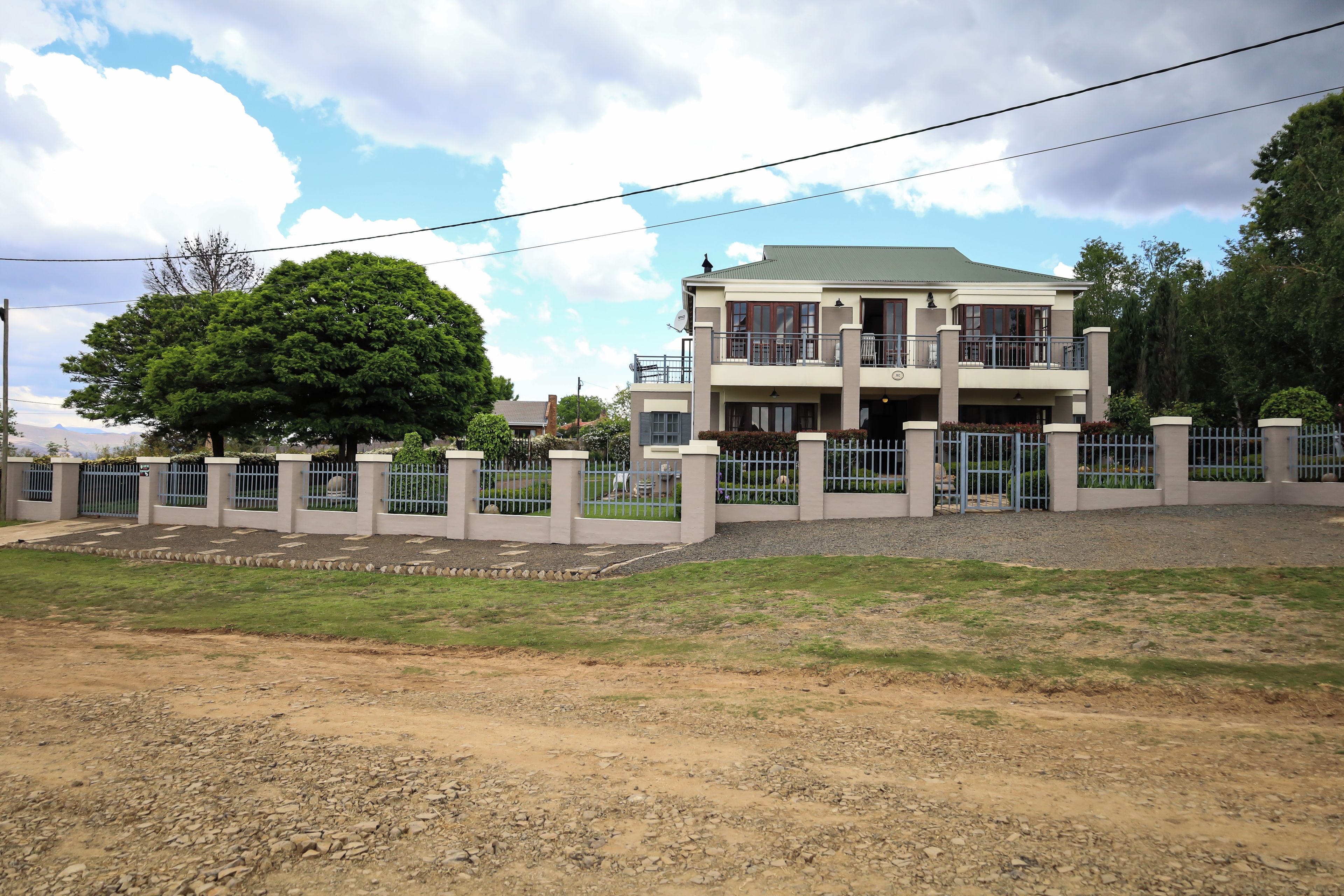 A two-story building with a balcony, surrounded by a fence and a large tree.