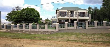 A two-story building with a balcony, surrounded by a fence and a large tree.