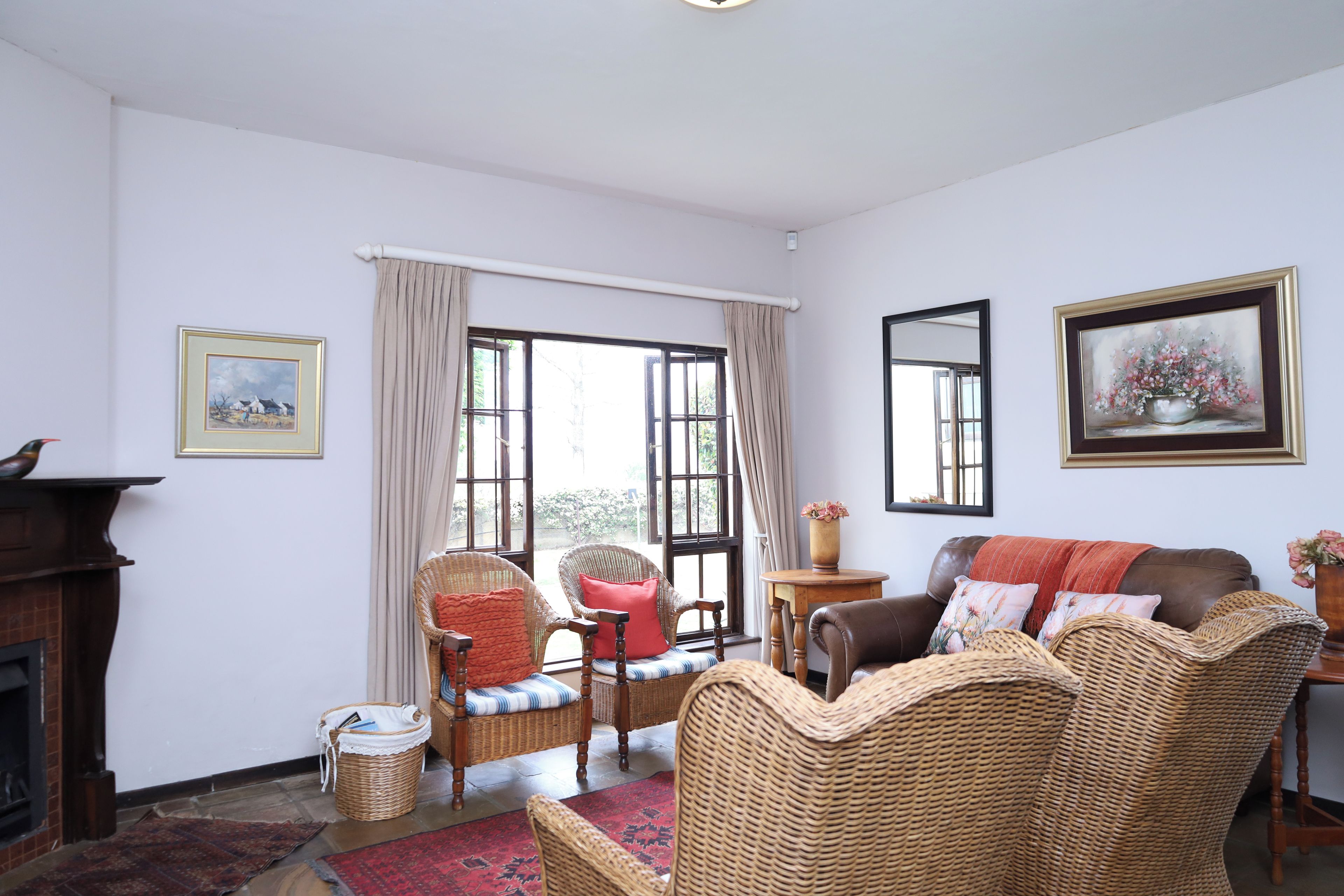 A room with wicker furniture, a fireplace, and a large window with curtains.